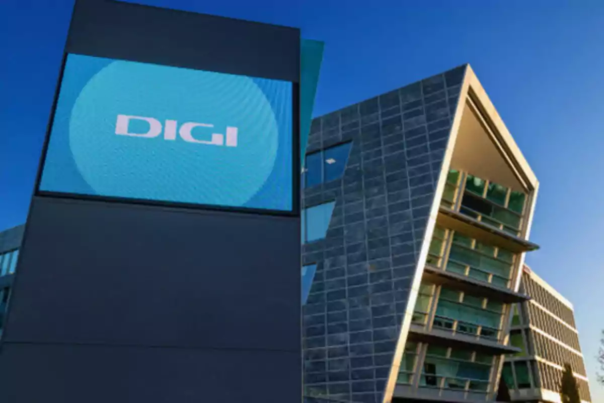 Edificio moderno con fachada de vidrio y un letrero digital que muestra el logo de DIGI bajo un cielo despejado Edificio moderno con fachada de vidrio y un letrero digital que muestra el logo de DIGI bajo un cielo despejado