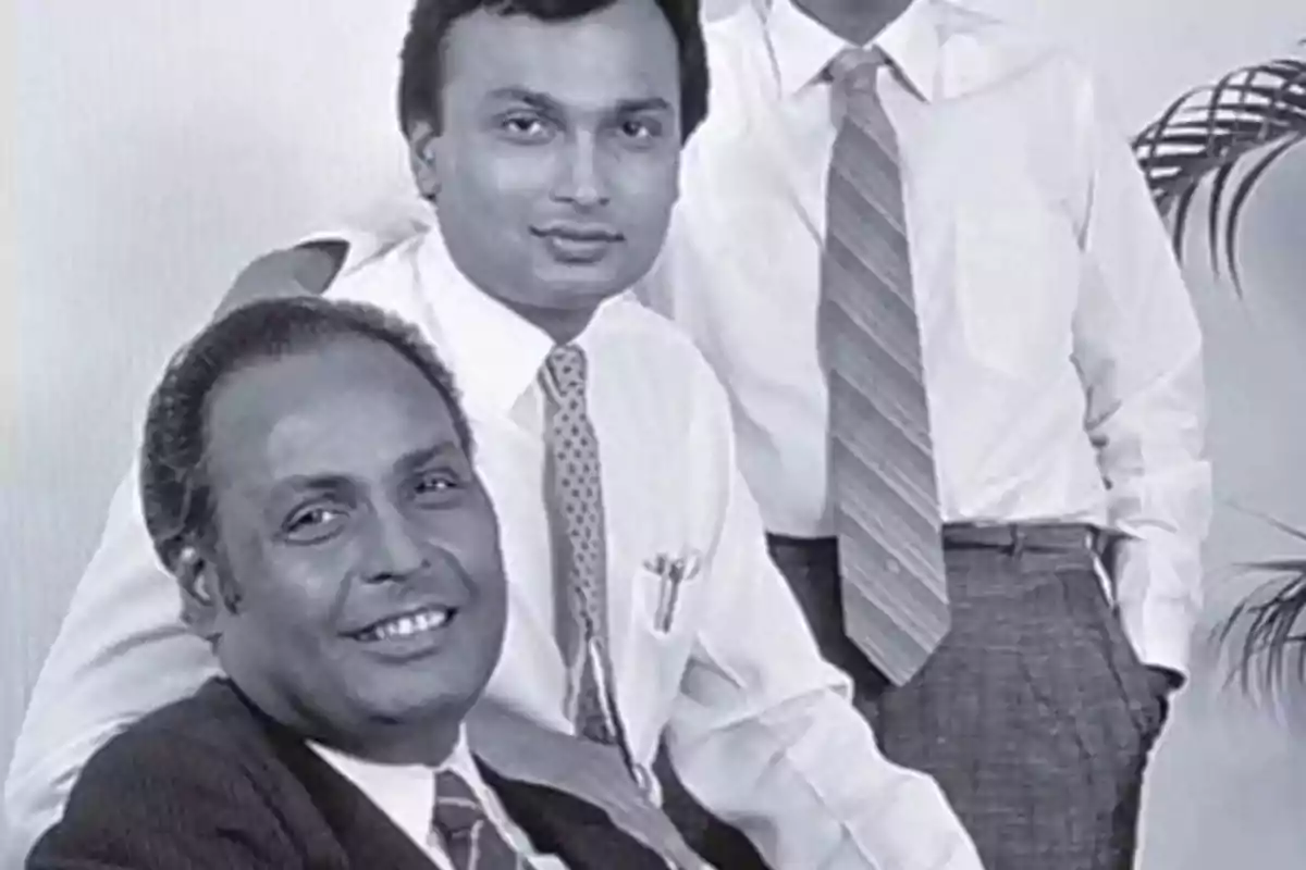 Tres hombres posan juntos en una fotografía en blanco y negro, todos vestidos con camisa y corbata, uno de ellos está sentado y los otros dos de pie Tres hombres posan juntos en una fotografía en blanco y negro, todos vestidos con camisa y corbata, uno de ellos está sentado y los otros dos de pie