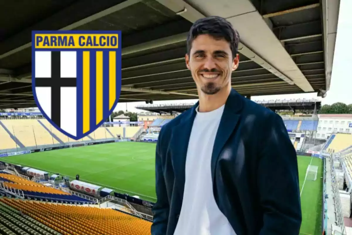 Hombre sonriente con chaqueta oscura en un estadio de fútbol con el escudo de Parma Calcio al fondo