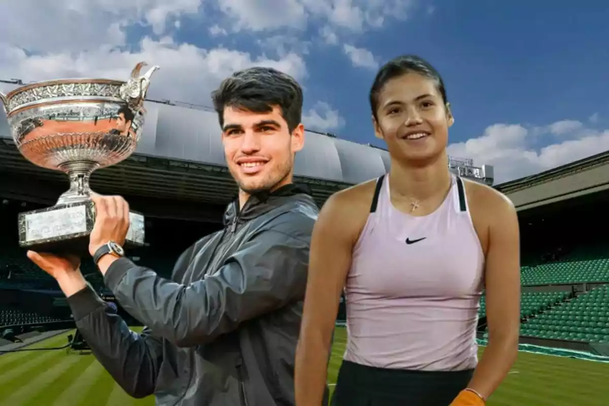Dos tenistas posan en una cancha de tenis, uno de ellos sostiene un trofeo grande y plateado mientras sonríe, la otra tenista está de pie a su lado con ropa deportiva y también sonríe, el cielo está despejado y las gradas del estadio están vacías.