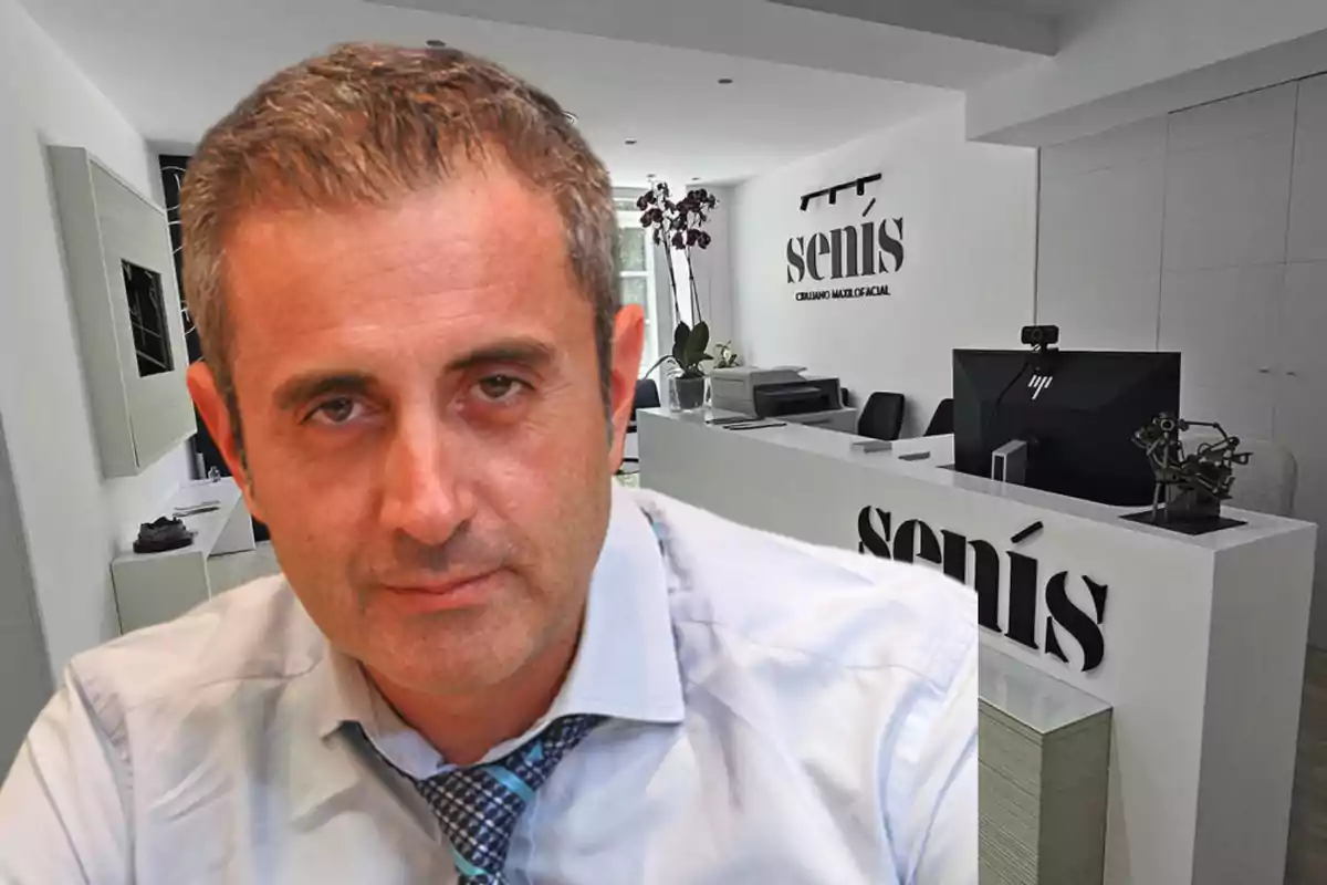 Hombre de cabello corto y canoso con camisa y corbata en primer plano frente a una recepción moderna de consultorio médico con el letrero senís en la pared