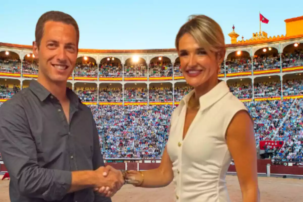 Dos personas sonrientes se dan la mano en el centro de una plaza de toros llena de público