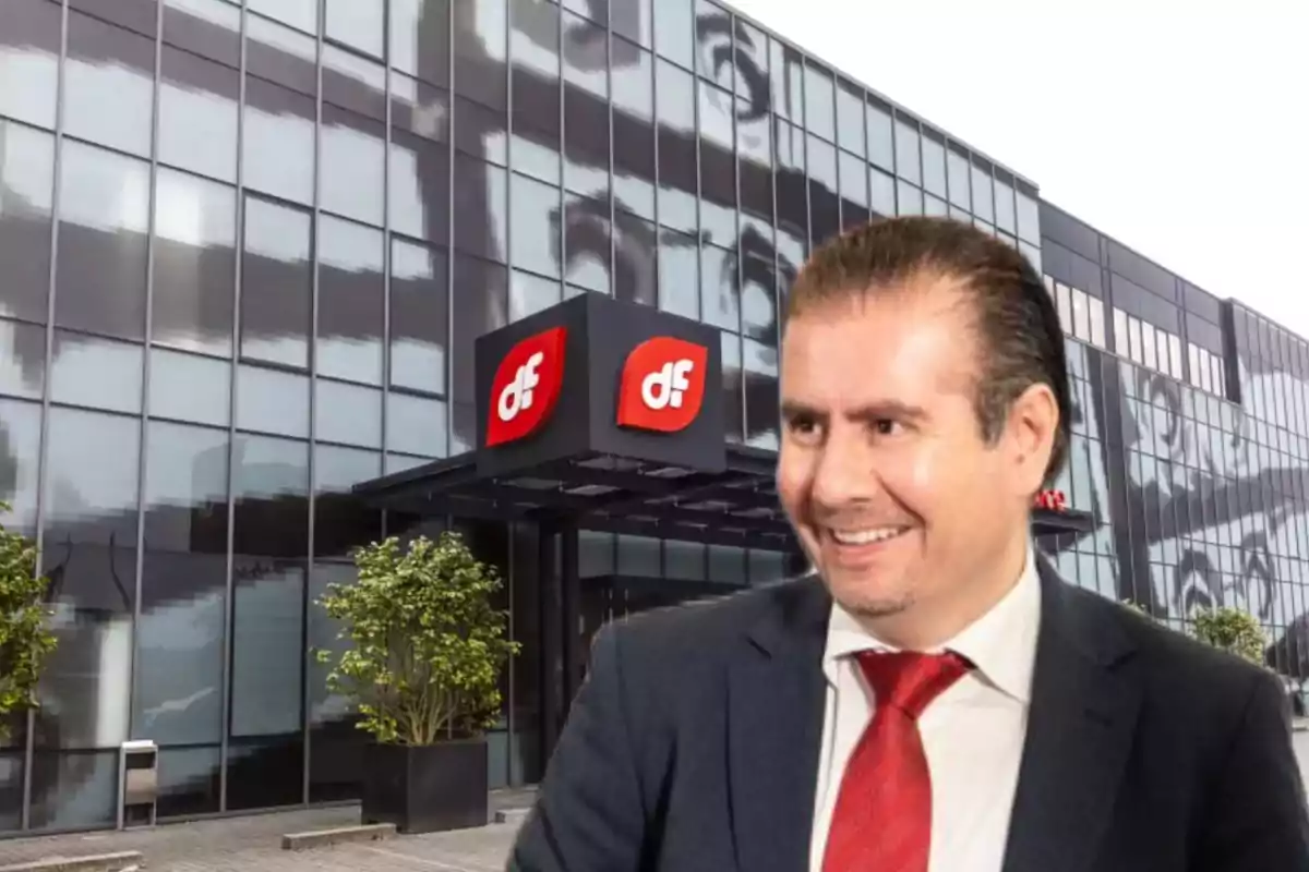 Hombre con traje y corbata roja sonriendo frente a un edificio de oficinas con logotipo rojo y blanco de df