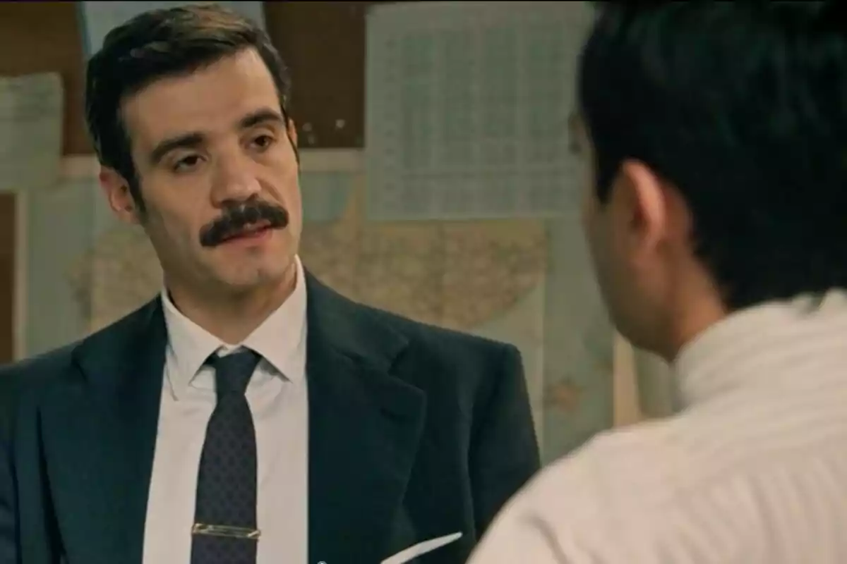 Javier Beltrán en una escena de 'Sueños de Libertad' con bigote y traje oscuro conversando con otra persona en una oficina. Javier Beltrán en una escena de 'Sueños de Libertad' con bigote y traje oscuro conversando con otra persona en una oficina.