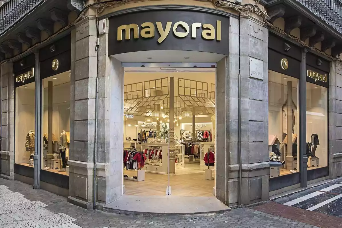 Fachada de una tienda de ropa Mayoral con vitrinas y entrada principal en una esquina de una calle peatonal Fachada de una tienda de ropa Mayoral con vitrinas y entrada principal en una esquina de una calle peatonal