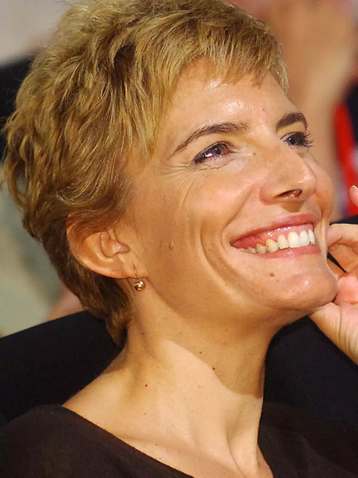 Mujer de cabello corto y rubio sonriendo mientras mira hacia un lado