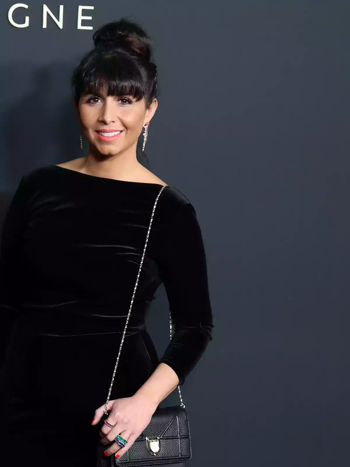 Mujer con vestido negro de terciopelo, bolso negro y peinado recogido, posando frente a un fondo gris oscuro
