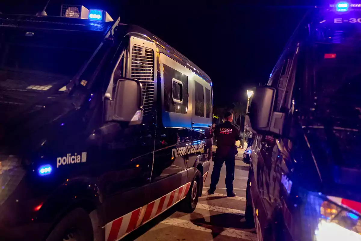 Furgones policiales con luces encendidas y un agente de espaldas en una calle de noche Furgones policiales con luces encendidas y un agente de espaldas en una calle de noche