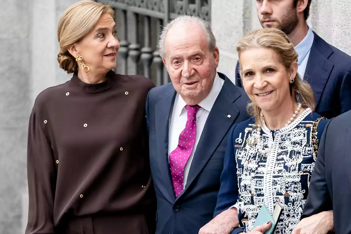 Tres personas elegantemente vestidas posan juntas y sonríen al aire libre frente a una pared de piedra Tres personas elegantemente vestidas posan juntas y sonríen al aire libre frente a una pared de piedra