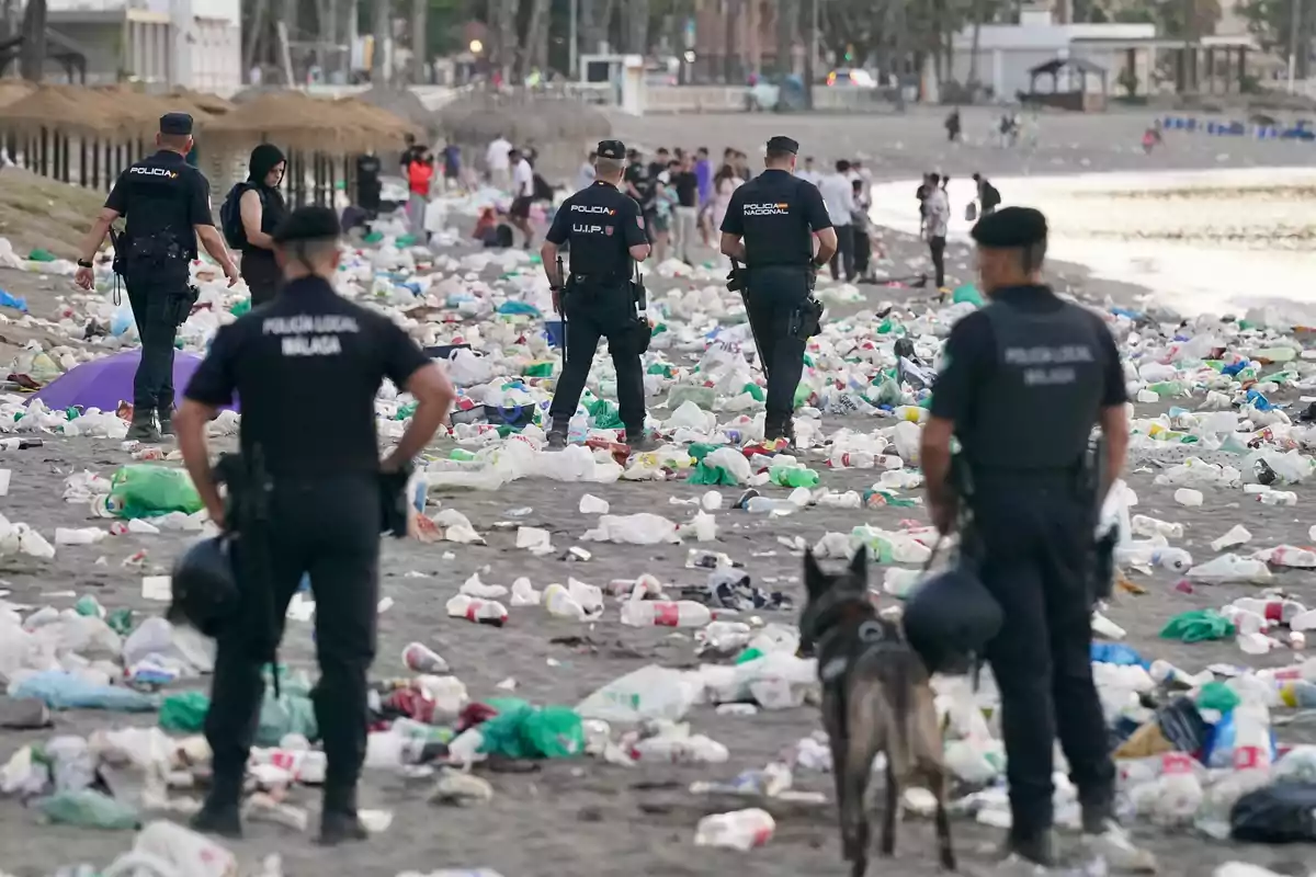 Varios policías caminan por una playa llena de basura y botellas de plástico mientras algunas personas observan a lo lejos Varios policías caminan por una playa llena de basura y botellas de plástico mientras algunas personas observan a lo lejos