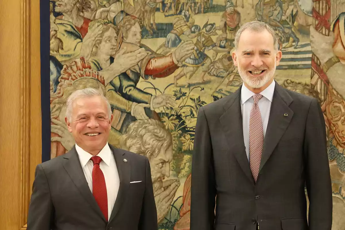 Dos hombres de traje sonríen frente a un tapiz decorativo antiguo Dos hombres de traje sonríen frente a un tapiz decorativo antiguo