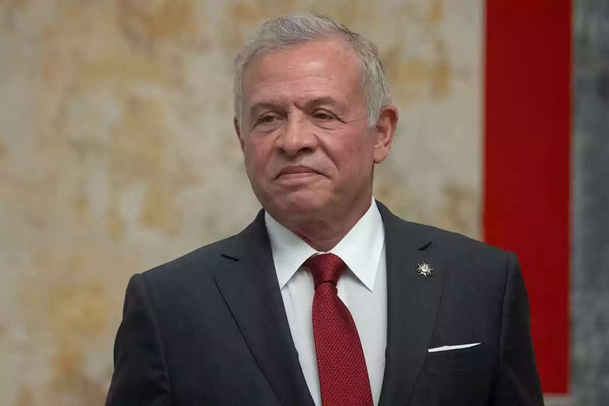 Hombre de cabello canoso con traje oscuro y corbata roja posando frente a un fondo desenfocado Hombre de cabello canoso con traje oscuro y corbata roja posando frente a un fondo desenfocado