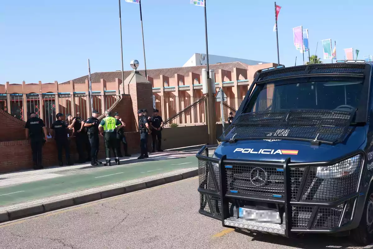 Varios policías y un vehículo policial están frente a un edificio de ladrillo bajo un cielo despejado Varios policías y un vehículo policial están frente a un edificio de ladrillo bajo un cielo despejado