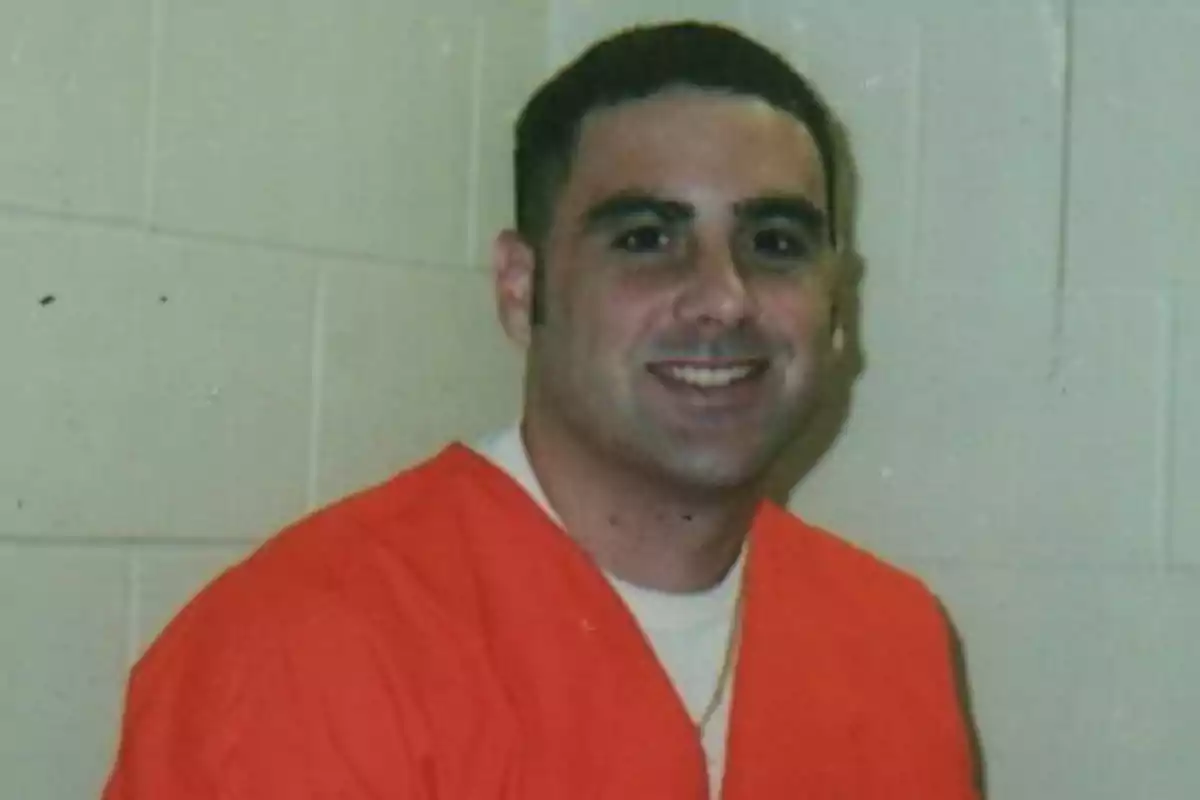 Hombre joven con cabello corto y oscuro, sonriente, vistiendo un uniforme naranja frente a una pared clara