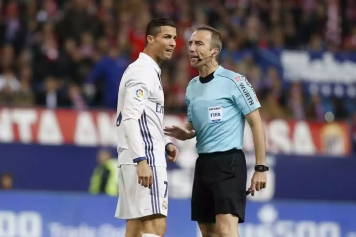 Un jugador de fútbol con uniforme blanco conversa con un árbitro vestido de celeste en medio de un partido Un jugador de fútbol con uniforme blanco conversa con un árbitro vestido de celeste en medio de un partido