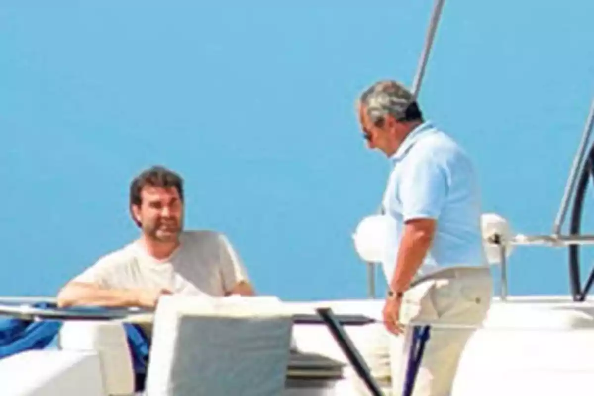 Dos hombres conversan a bordo de un yate bajo un cielo despejado Dos hombres conversan a bordo de un yate bajo un cielo despejado