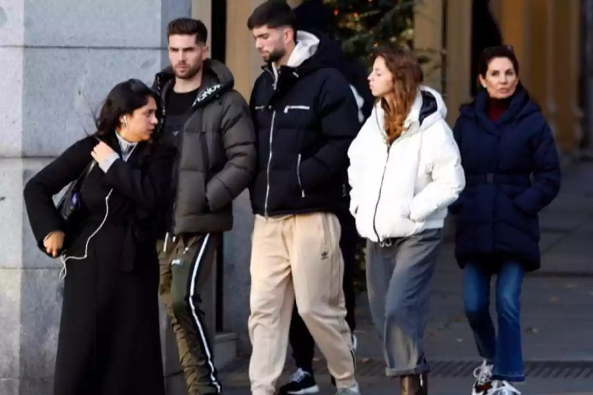 Cinco personas con ropa de invierno caminan por una acera en una ciudad