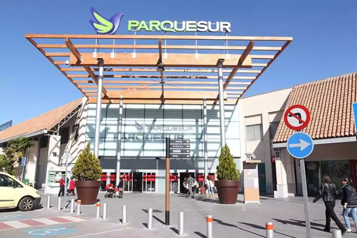 Entrada principal del centro comercial Parquesur con personas caminando y señales de tráfico visibles bajo un cielo despejado Entrada principal del centro comercial Parquesur con personas caminando y señales de tráfico visibles bajo un cielo despejado