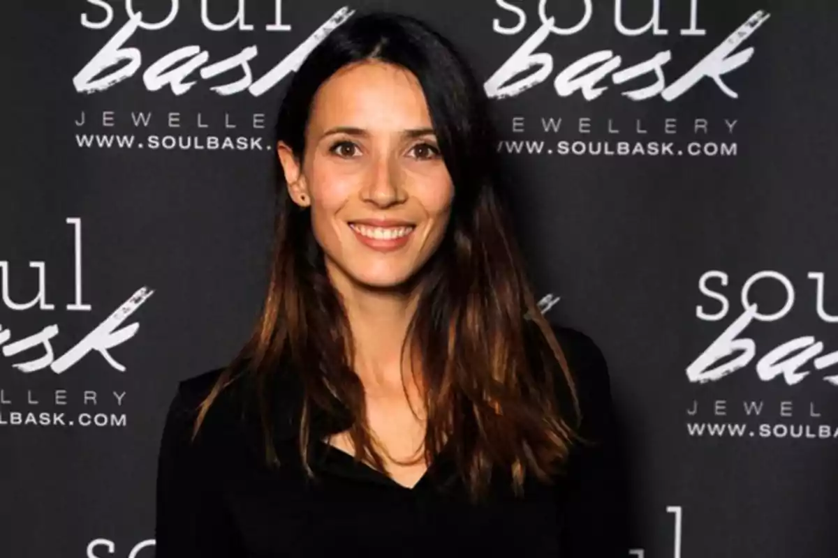 Mujer de cabello largo y oscuro sonriendo frente a un fondo promocional de la marca Soul Bask Mujer de cabello largo y oscuro sonriendo frente a un fondo promocional de la marca Soul Bask