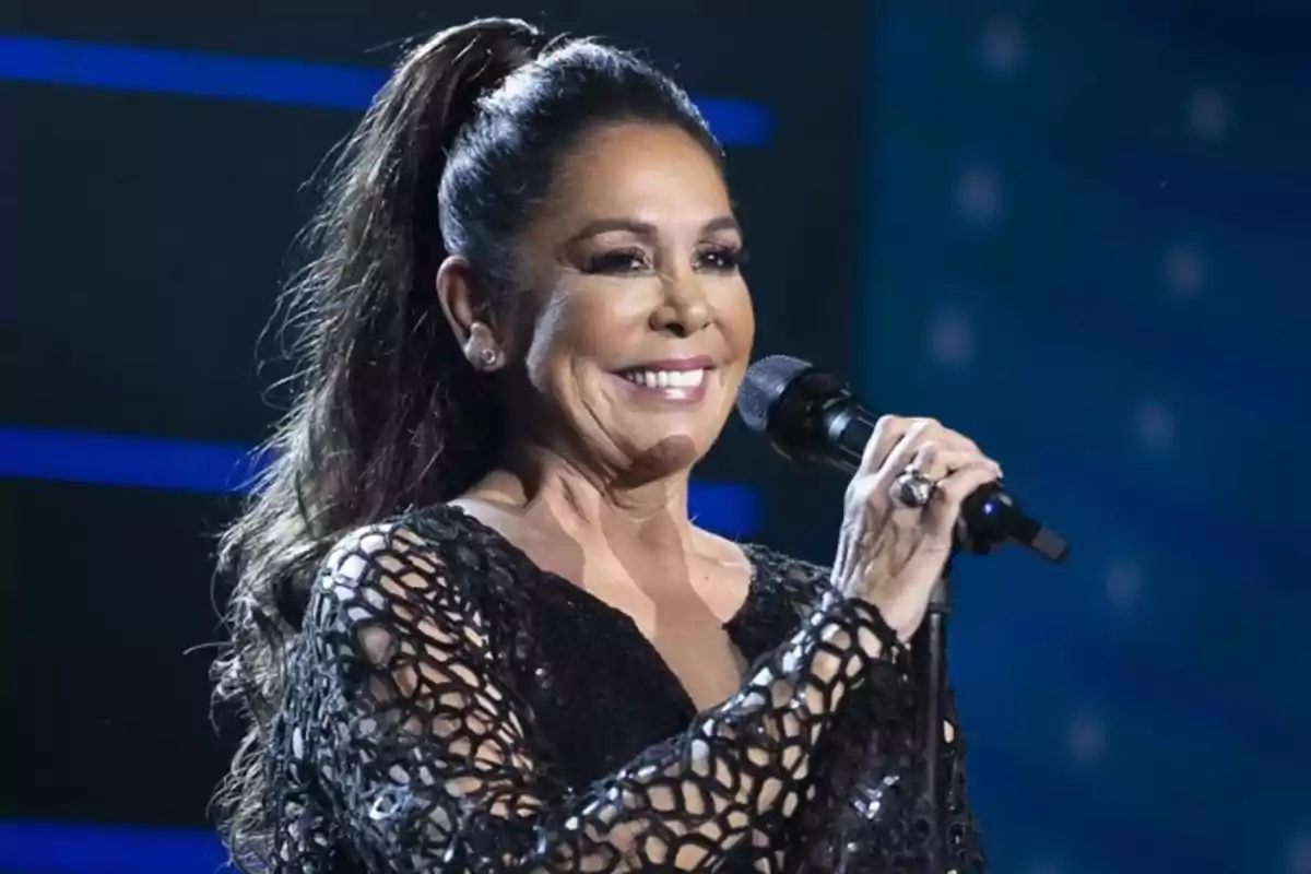 Mujer sonriente con el cabello recogido cantando en un escenario y sosteniendo un micrófono Mujer sonriente con el cabello recogido cantando en un escenario y sosteniendo un micrófono