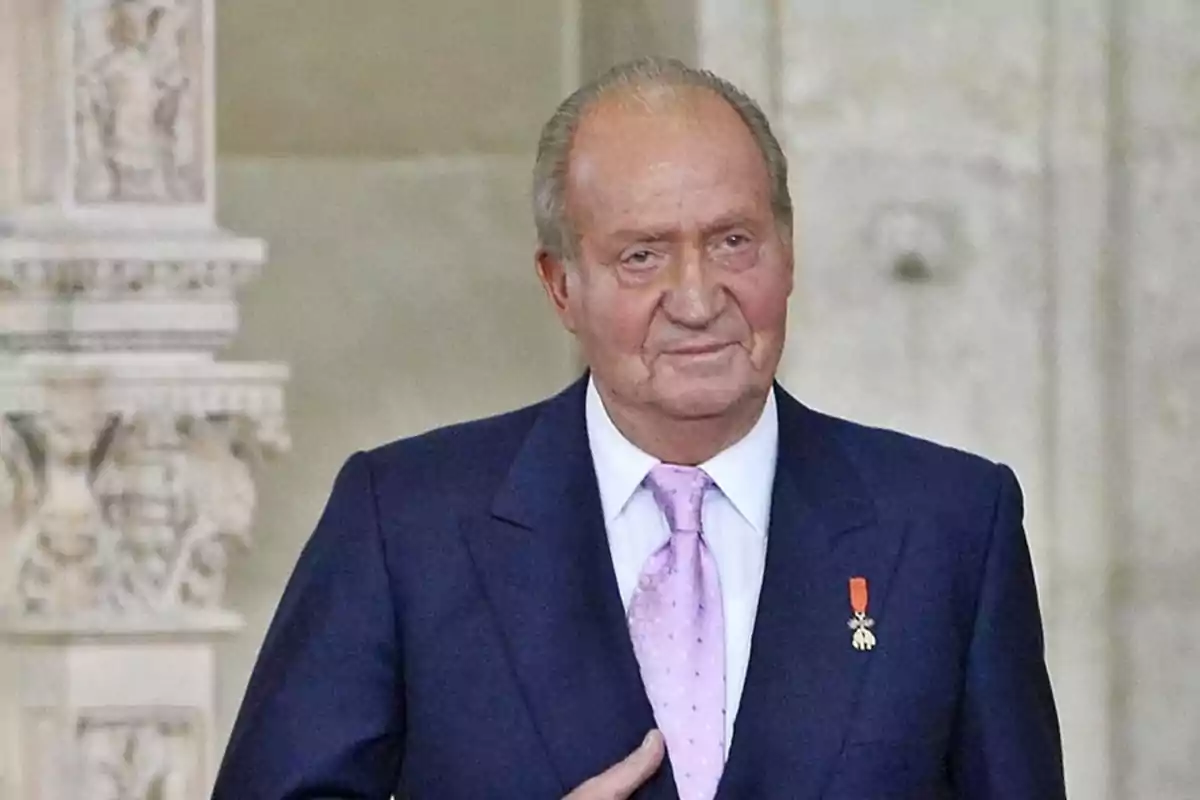 Hombre mayor con traje azul y corbata rosa posando en un entorno elegante con columnas decorativas al fondo Hombre mayor con traje azul y corbata rosa posando en un entorno elegante con columnas decorativas al fondo