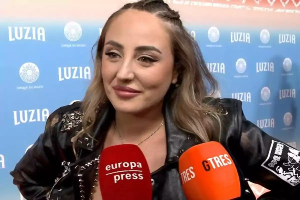 Mujer con chaqueta de cuero siendo entrevistada por varios medios frente a un fondo azul con el logo de Luzia Cirque du Soleil Mujer con chaqueta de cuero siendo entrevistada por varios medios frente a un fondo azul con el logo de Luzia Cirque du Soleil