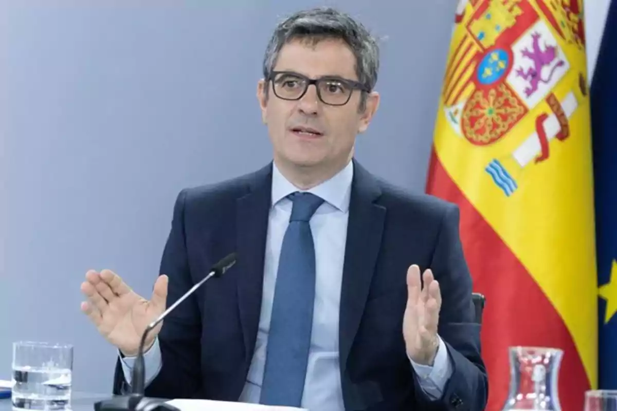 Hombre con gafas y traje azul hablando en una conferencia con la bandera de España de fondo Hombre con gafas y traje azul hablando en una conferencia con la bandera de España de fondo
