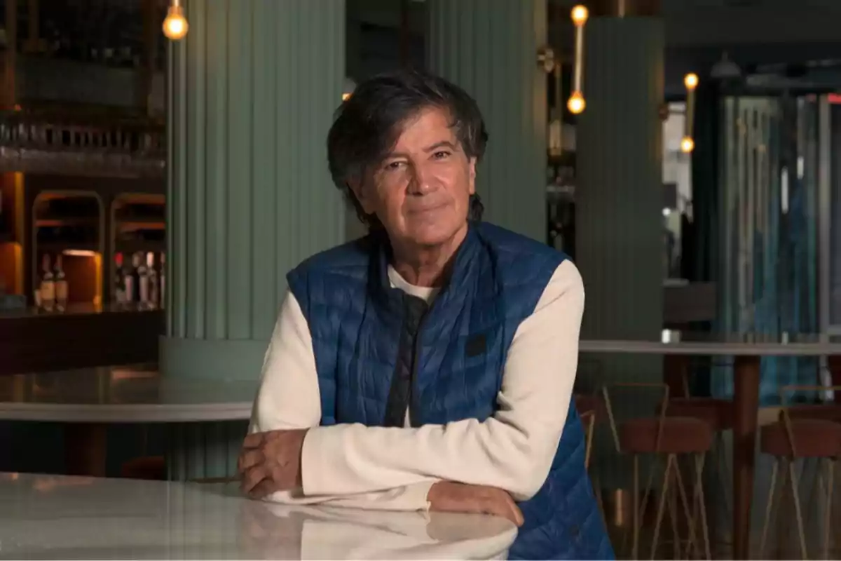 Hombre de cabello canoso y chaleco azul sentado en una mesa dentro de un restaurante elegante Hombre de cabello canoso y chaleco azul sentado en una mesa dentro de un restaurante elegante