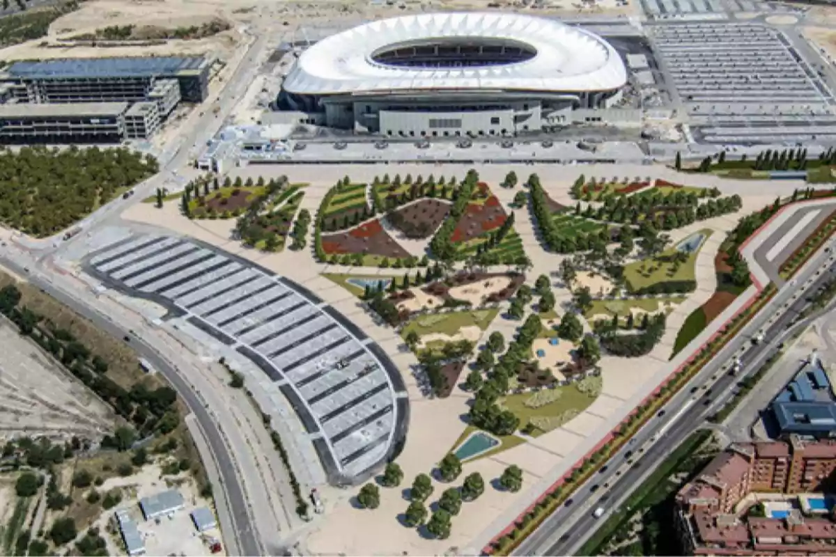 Vista aérea de un estadio moderno rodeado de jardines, áreas verdes, caminos peatonales y estacionamientos, con avenidas y edificios residenciales en los alrededores Vista aérea de un estadio moderno rodeado de jardines, áreas verdes, caminos peatonales y estacionamientos, con avenidas y edificios residenciales en los alrededores