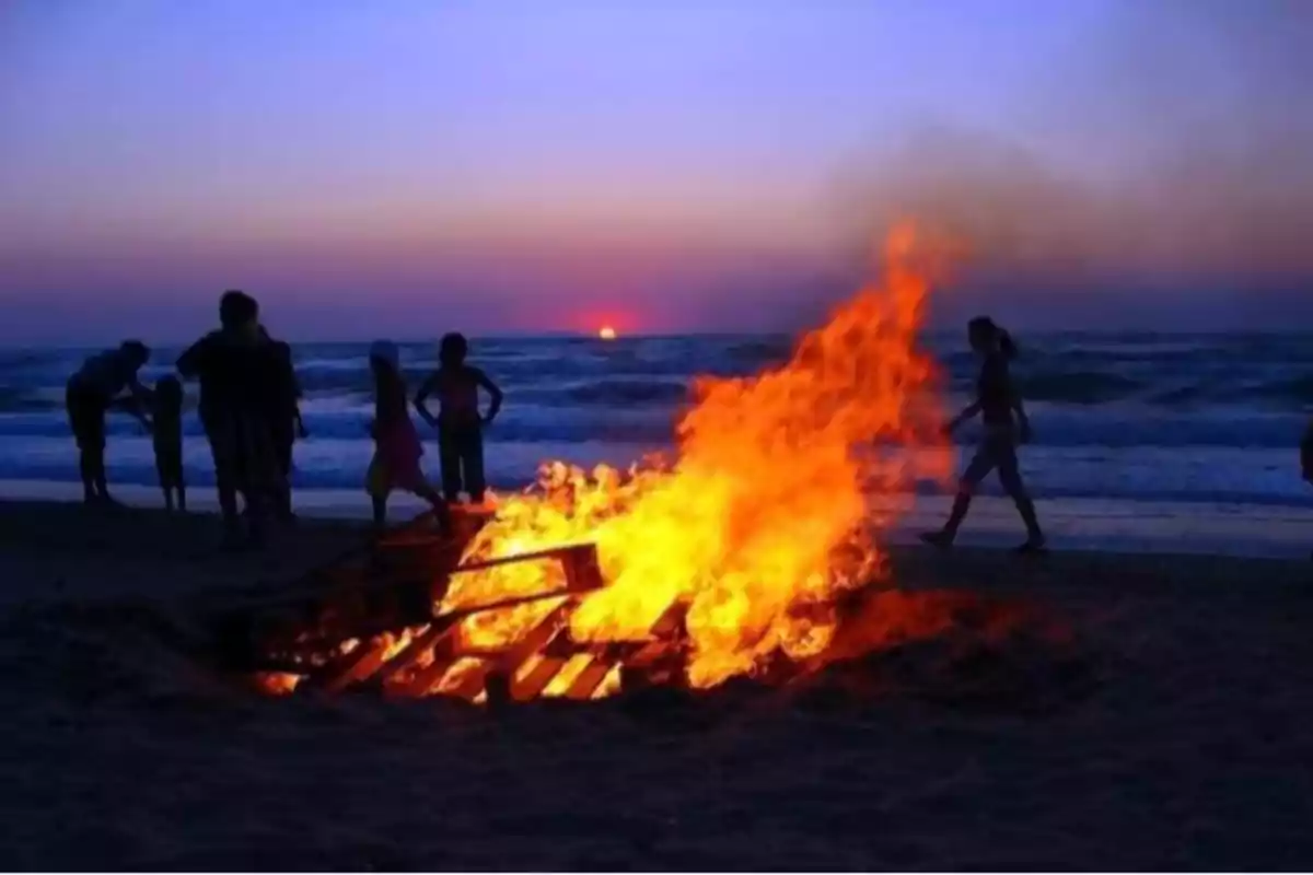 Personas reunidas alrededor de una fogata en la playa al atardecer con el mar de fondo