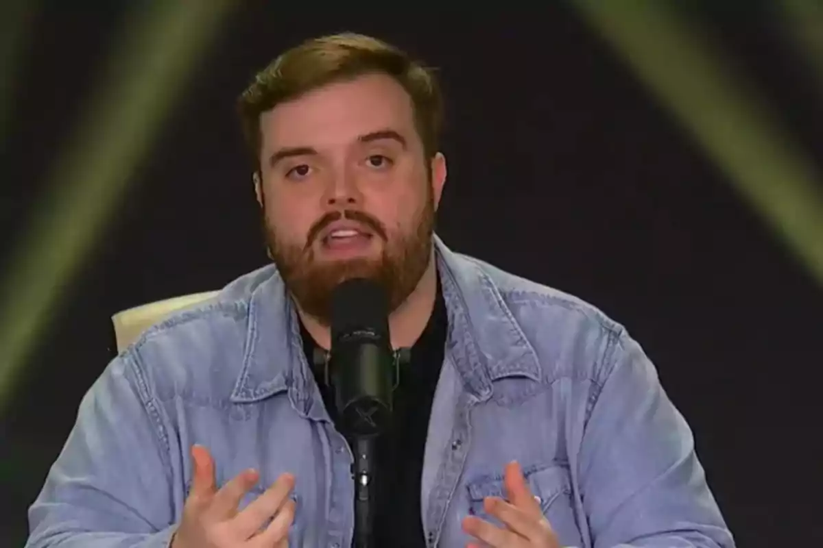 Hombre con barba y chaqueta de mezclilla hablando frente a un micrófono Hombre con barba y chaqueta de mezclilla hablando frente a un micrófono