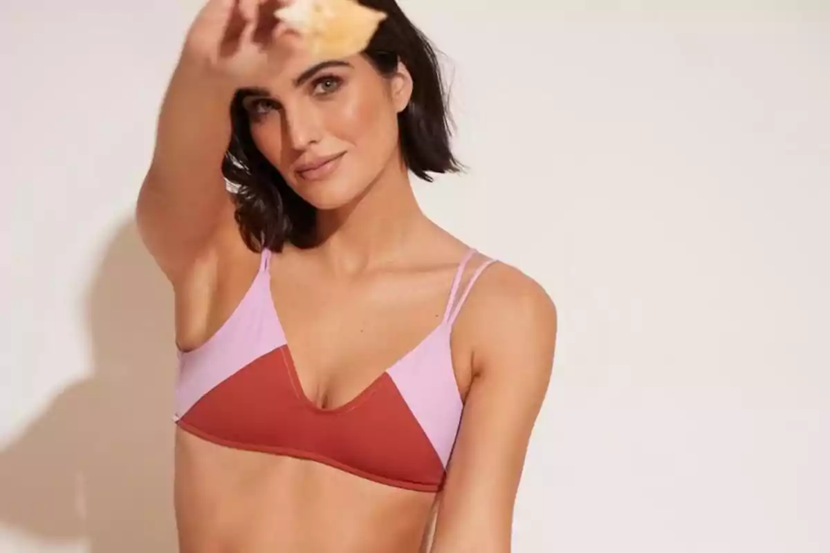 Mujer de cabello corto y oscuro usando un bikini en tonos rosa y rojo, sosteniendo un objeto desenfocado frente a la cámara