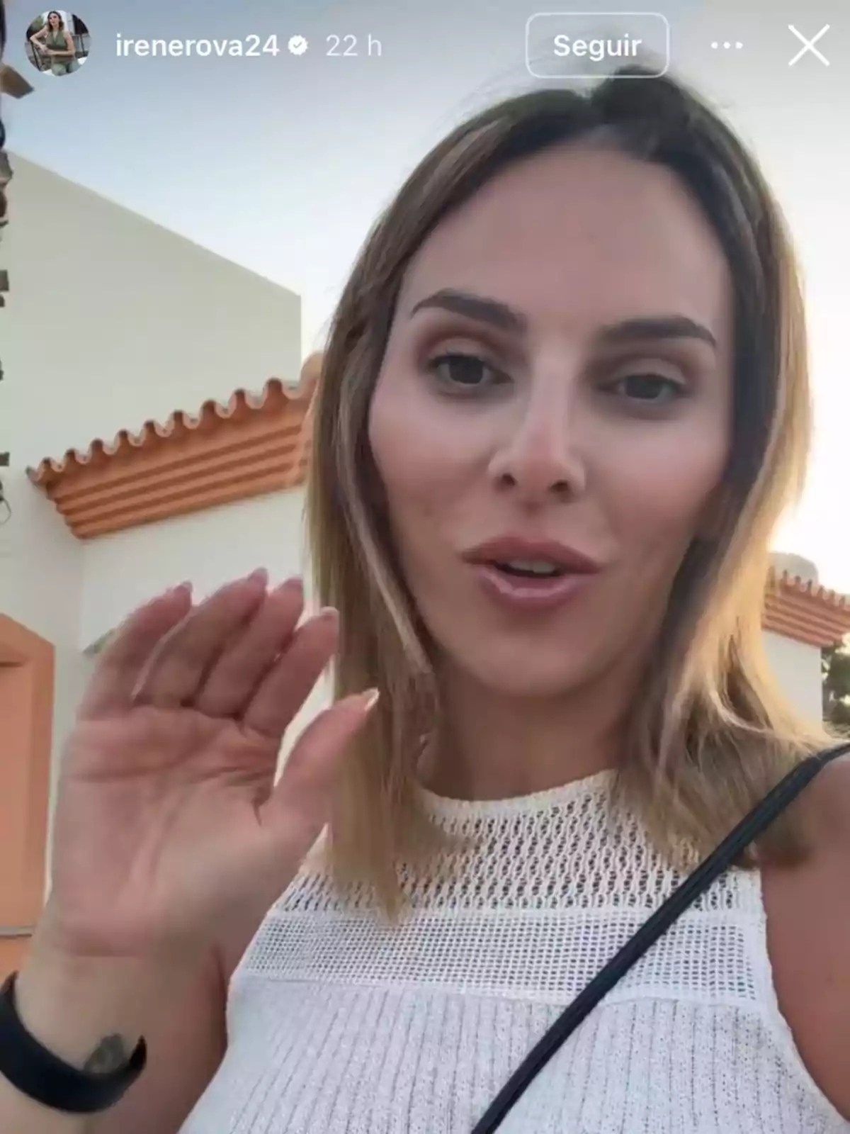Irene Rosales joven con cabello rubio oscuro y top blanco saluda a la cámara al aire libre frente a una casa de paredes claras y techo de tejas naranjas Irene Rosales joven con cabello rubio oscuro y top blanco saluda a la cámara al aire libre frente a una casa de paredes claras y techo de tejas naranjas