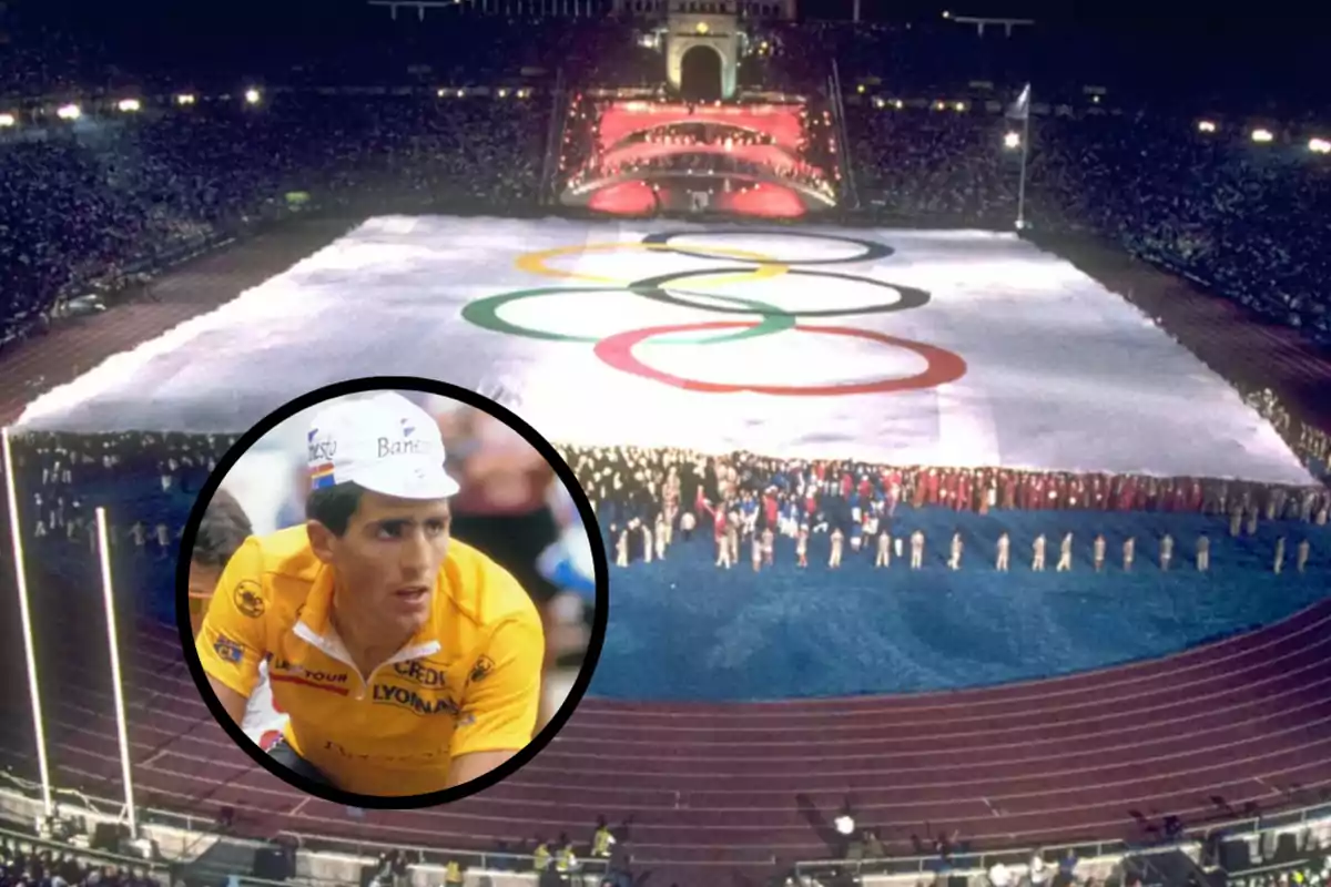 Un estadio olímpico lleno durante una ceremonia con una gran bandera de los anillos olímpicos en el centro y un ciclista con uniforme amarillo en un recuadro en primer plano