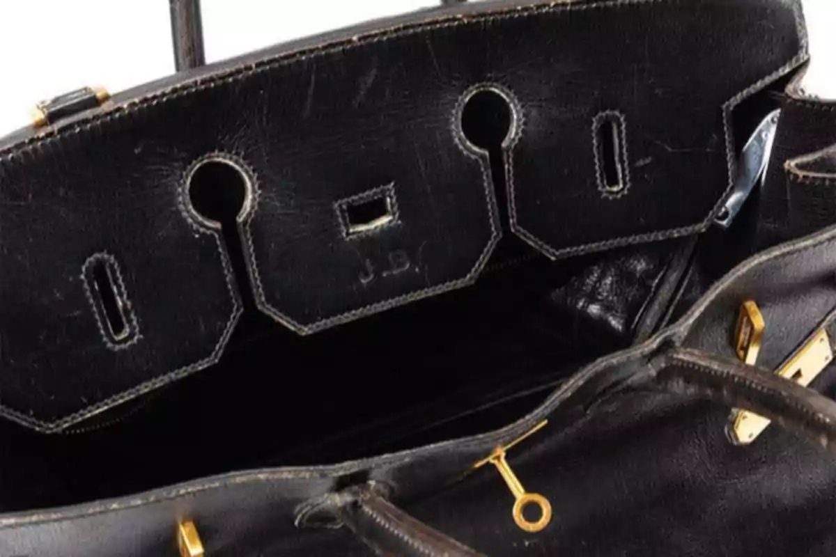 Bolso de cuero negro abierto con herrajes dorados y costuras visibles Bolso de cuero negro abierto con herrajes dorados y costuras visibles