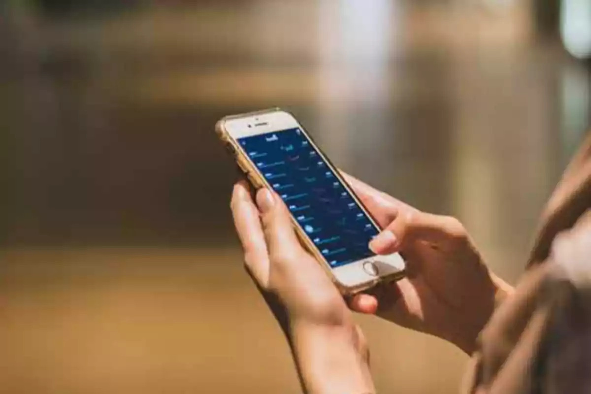 Persona sosteniendo un teléfono móvil con ambas manos mientras navega por una aplicación en la pantalla
