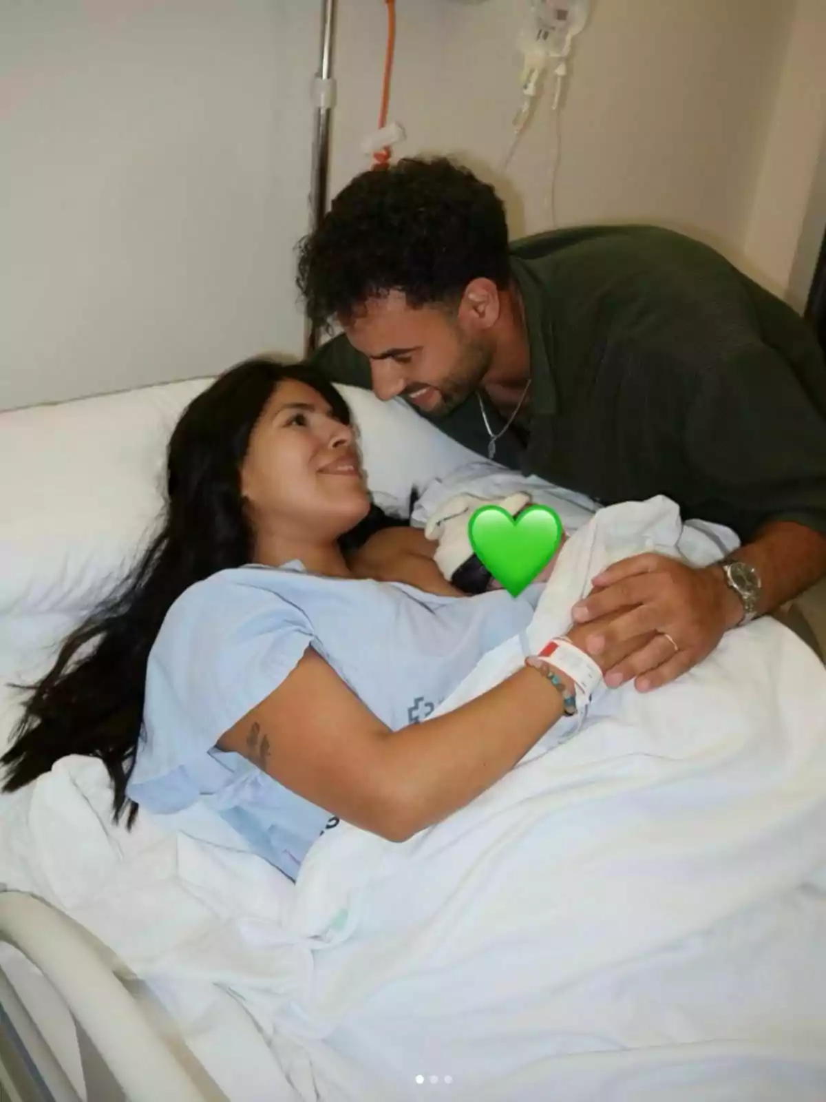 Isa Pantoja recostada en una cama de hospital sonríe mientras Asraf Beno la mira con ternura y ambos se toman de la mano, cubiertos por una sábana blanca. Isa Pantoja recostada en una cama de hospital sonríe mientras Asraf Beno la mira con ternura y ambos se toman de la mano, cubiertos por una sábana blanca.