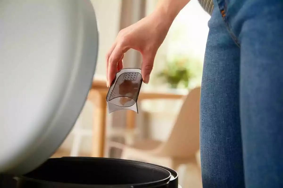 Persona tirando un filtro de café usado en un bote de basura en una cocina.