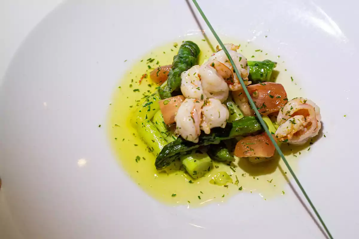 Camarones salteados con espárragos y trozos de jitomate en salsa de aceite de oliva, decorados con hierbas finas en un plato blanco Camarones salteados con espárragos y trozos de jitomate en salsa de aceite de oliva, decorados con hierbas finas en un plato blanco