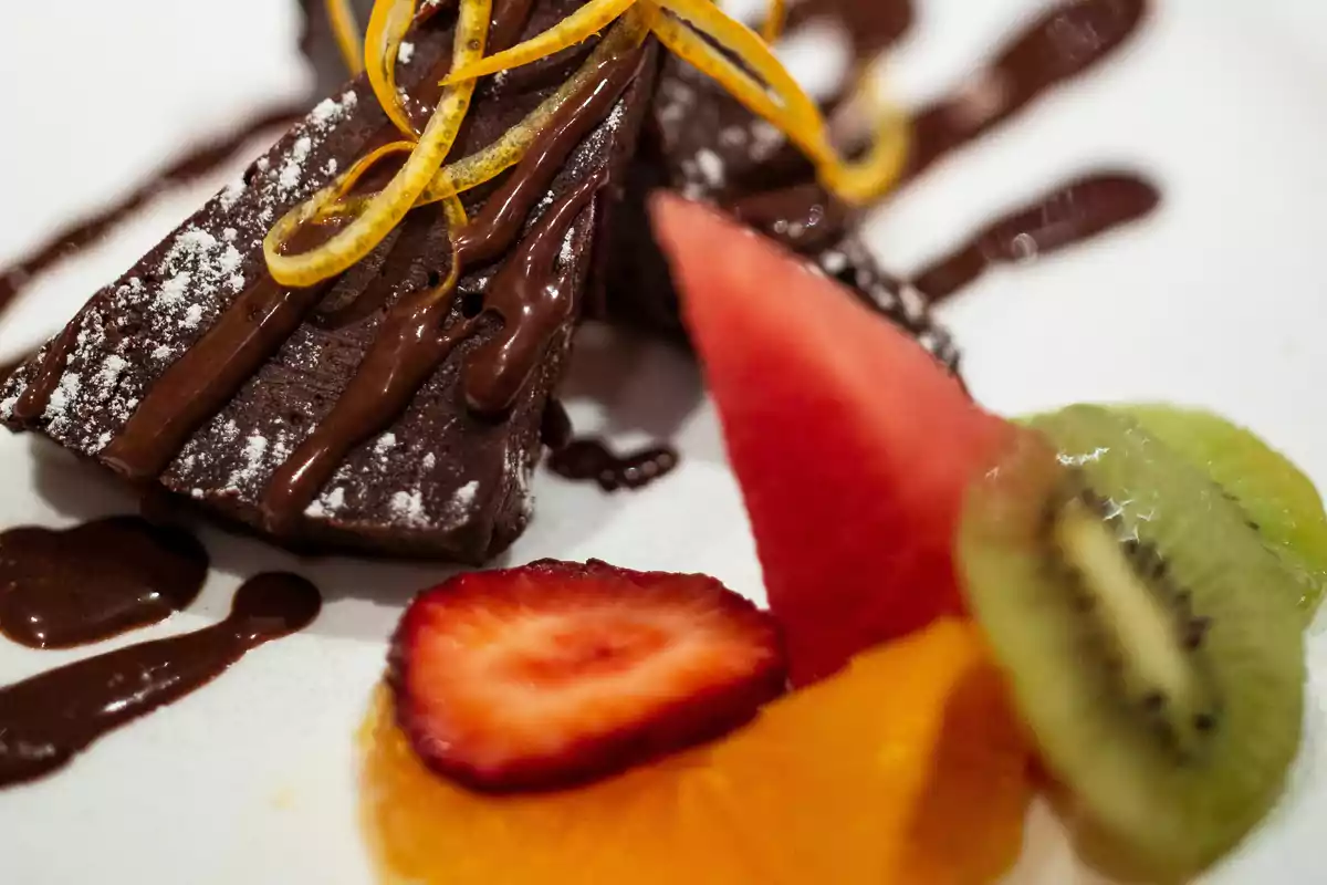 Postre de pastel de chocolate decorado con rodajas de naranja y acompañado de frutas frescas como fresa, kiwi, naranja y sandía Postre de pastel de chocolate decorado con rodajas de naranja y acompañado de frutas frescas como fresa, kiwi, naranja y sandía