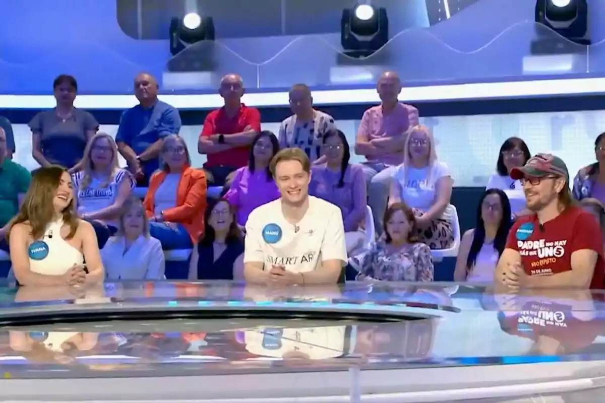 Tres concursantes -uno de ellos Manu Pascual- sentados en una mesa redonda sonríen mientras participan en un programa de televisión con público al fondo. Tres concursantes -uno de ellos Manu Pascual- sentados en una mesa redonda sonríen mientras participan en un programa de televisión con público al fondo.