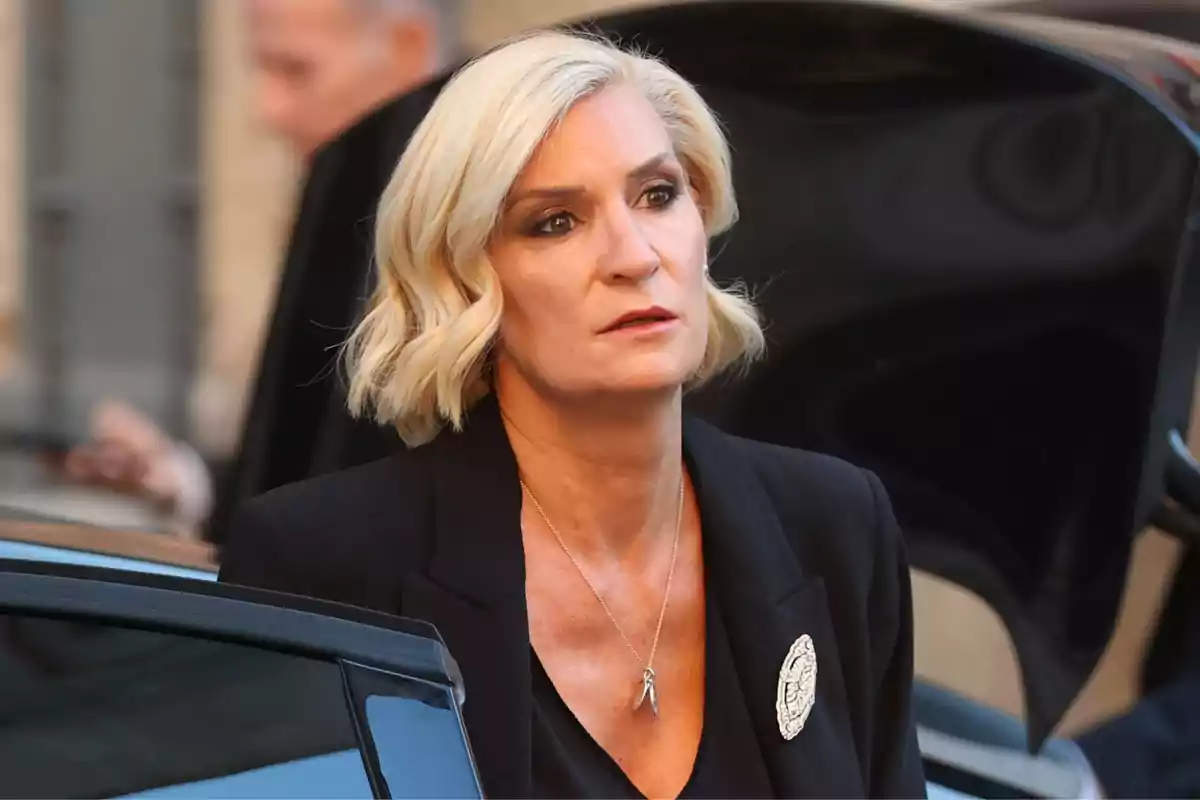 Mujer rubia de cabello corto con expresión seria vestida de negro saliendo de un automóvil Mujer rubia de cabello corto con expresión seria vestida de negro saliendo de un automóvil