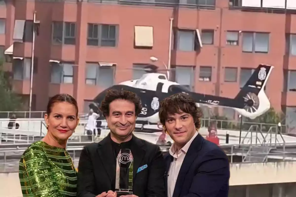 Tres personas posan sonrientes al frente mientras sostienen un trofeo, detrás de ellas hay un helicóptero de la policía en la azotea de un edificio.