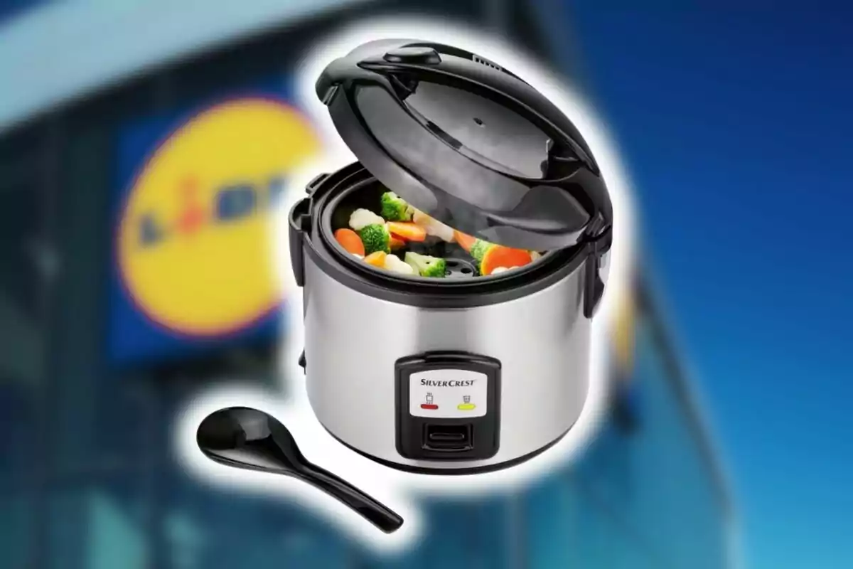 Olla arrocera eléctrica con tapa abierta de Lidl mostrando verduras en su interior y una cuchara negra al frente con el logo de una tienda de fondo desenfocado. Olla arrocera eléctrica con tapa abierta de Lidl mostrando verduras en su interior y una cuchara negra al frente con el logo de una tienda de fondo desenfocado.