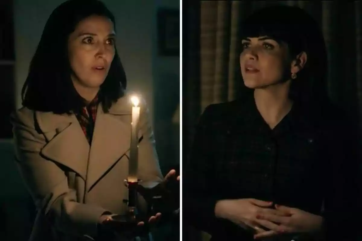 Luz y Gema en una habitación oscura, una sostiene una vela encendida y parece sorprendida, la otra la observa con expresión seria.