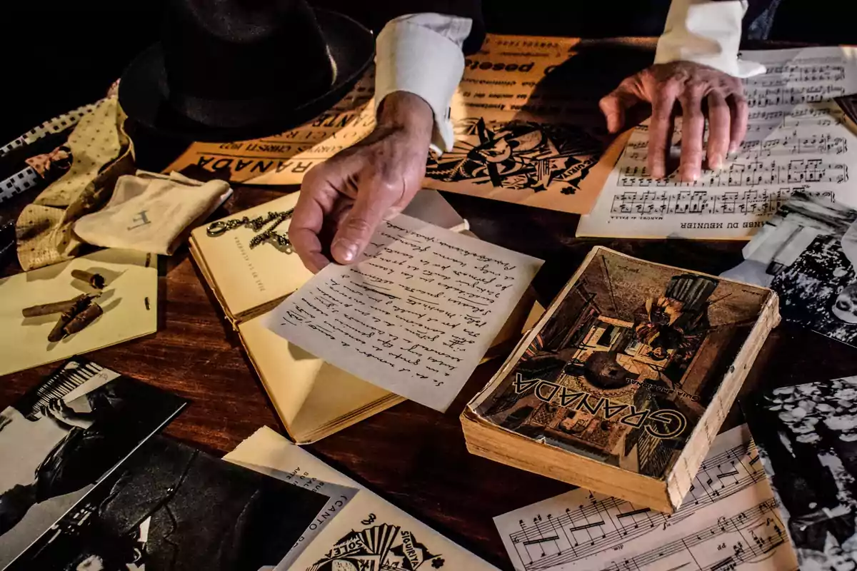 Manos de una persona revisando cartas, partituras, fotografías antiguas y objetos personales sobre una mesa de madera Manos de una persona revisando cartas, partituras, fotografías antiguas y objetos personales sobre una mesa de madera