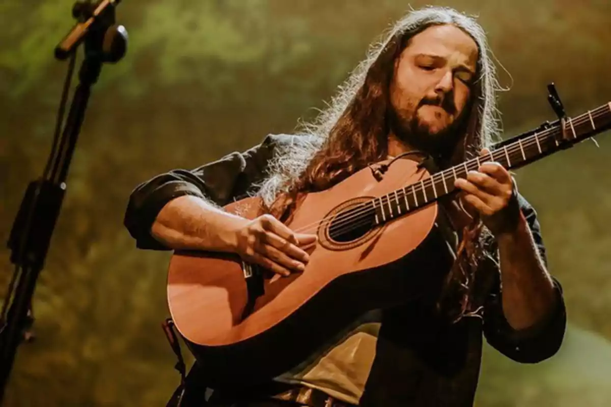 Hombre con cabello largo tocando una guitarra en un escenario iluminado
