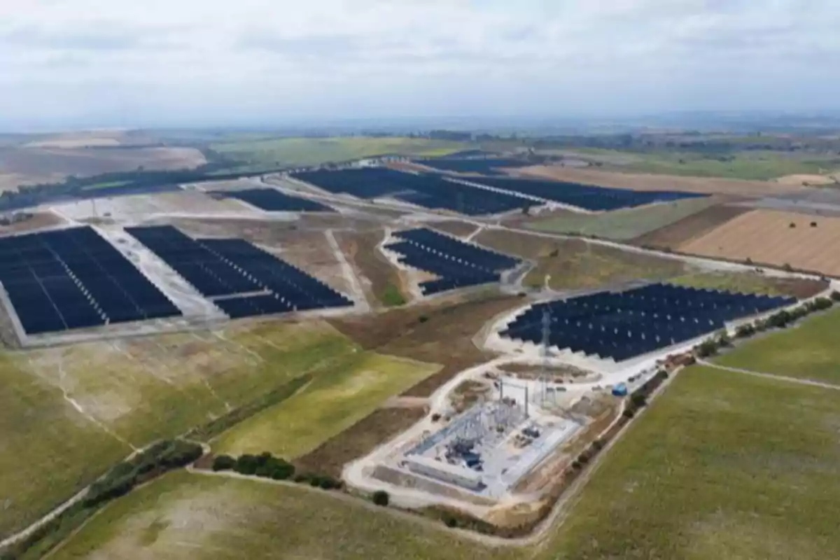 Vista aérea de un extenso campo con paneles solares organizados en filas sobre terrenos rurales rodeados de vegetación y caminos de tierra Vista aérea de un extenso campo con paneles solares organizados en filas sobre terrenos rurales rodeados de vegetación y caminos de tierra