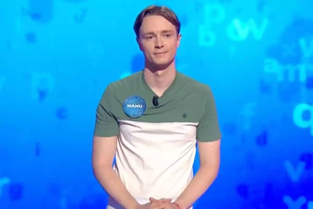 Manu con camiseta verde y blanca está de pie frente a un fondo azul con letras difuminadas y lleva una chapa azul con el nombre Manu. Captura de 'Pasapalabra' Manu con camiseta verde y blanca está de pie frente a un fondo azul con letras difuminadas y lleva una chapa azul con el nombre Manu. Captura de 'Pasapalabra'
