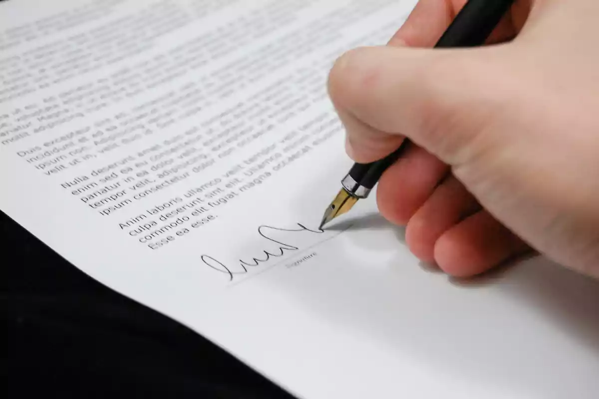 Persona firmando un documento con una pluma sobre una hoja de papel impresa
